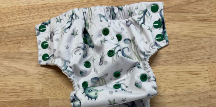 Young parent packing swim diapers into a beach bag next to baby floaties and sunscreen, preparing for baby’s first pool day.